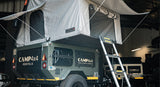 A pop up rooftop tent with ladder & bedding above a trailer.
