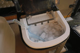 Ice maker with ice cubes and a scoop inside an appliance.