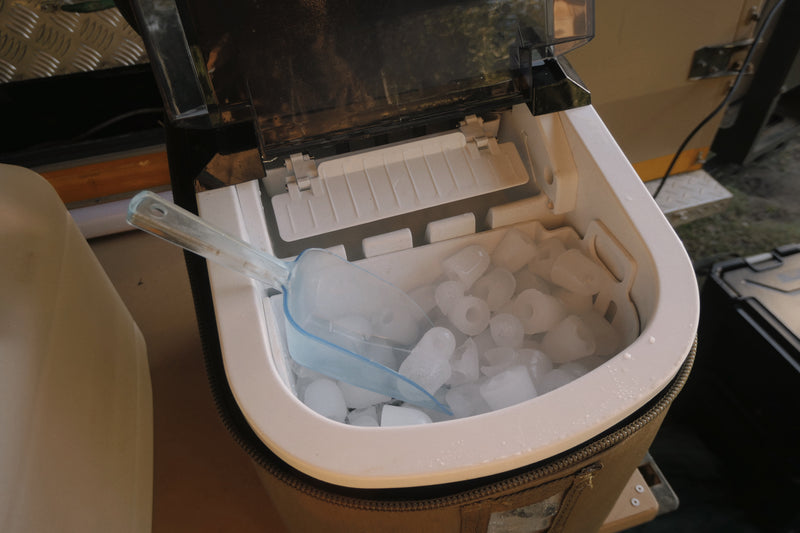 Ice maker with ice cubes and a scoop inside an appliance.