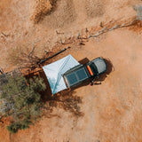 Aerial view of a car with an extended Alu-Cab 270 Shadow Awning,  solar panels on its roof parked in a desert landscape. Camp4x4. camp 4x4, overlanding, camping. Double Cab. Single Cab. Extra Cab