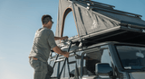 A man climbing a ladder to the Alu-Cab Rooftop Tent above Suzuki Jimny 4x4 for rent.
