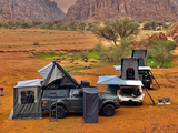 Alu-Cab 270 awning, with the Awning Side Wall Kit and a hard shell rooftop tent, fitted to a camping vehicle, with similar vehicles camping in the wilderness