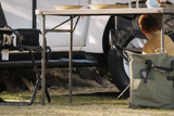 Camping scene with a camping table and chairs, and a child sitting on the grass below the table