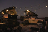 Two vehicles with rooftop tents under string lights.