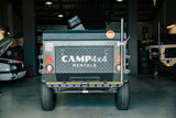 Back of a camper trailer with 'CAMP4x4 Rentals' branding in a garage setting.