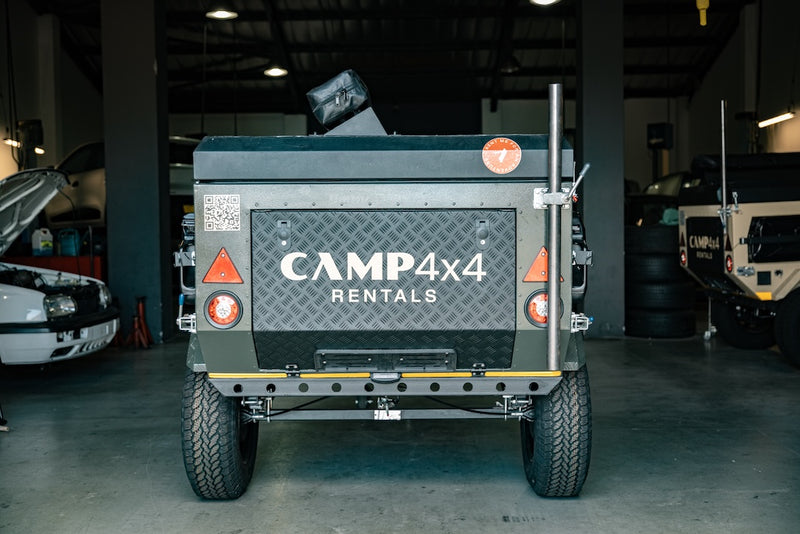 Back of a camper trailer with 'CAMP4x4 Rentals' branding in a garage setting.