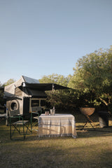 Camping trailer with rooftop tent in an outdoor setting including a table and chairs with champagne on ice for two.