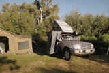 Camper van attached to a vehicle with a tent set up in a natural setting