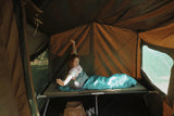 Person lying on a camping bed inside a tent with a scenic view outside